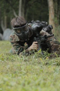 male playing paintball while laying the grass hiding from the enemy team