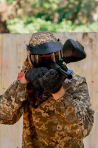 close up in the wild near tree structures a player in a pintball uniform holds a pistol with a red balloon team game camouflage clothing