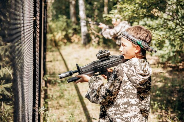 Boy looking into the optical sight a weapon. Children playing laser tag shooting game in outdoor. War simulation game